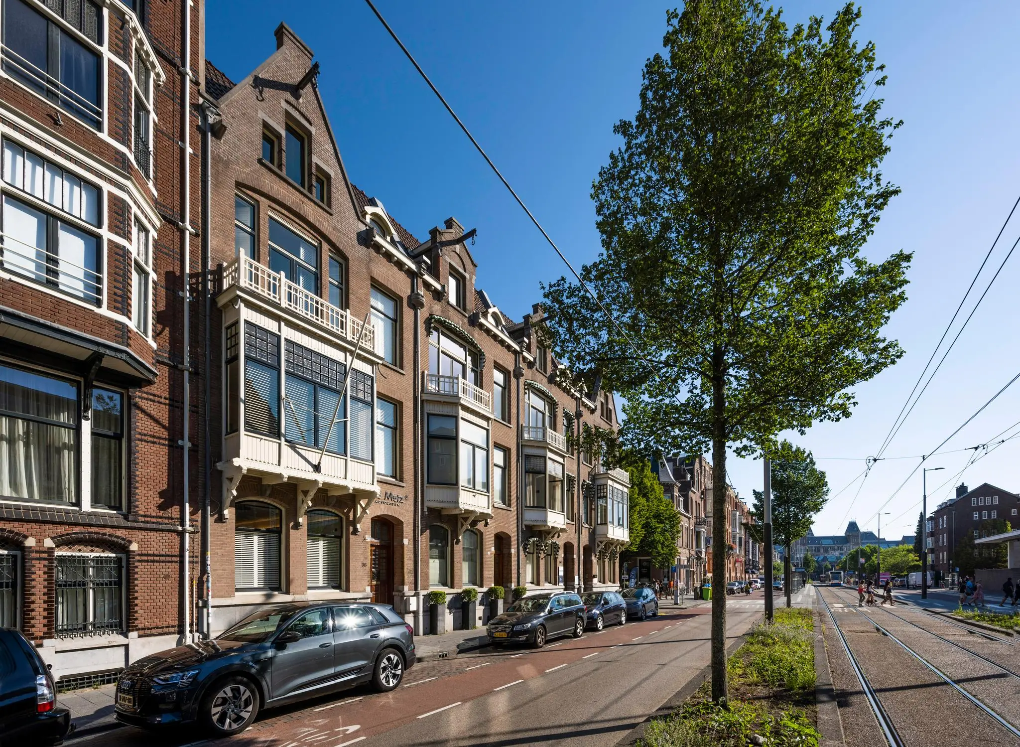 Rijtje statige herenhuizen aan de Paulus Potterstraat in Amsterdam met tramlijn en geparkeerde auto’s op een zonnige dag.